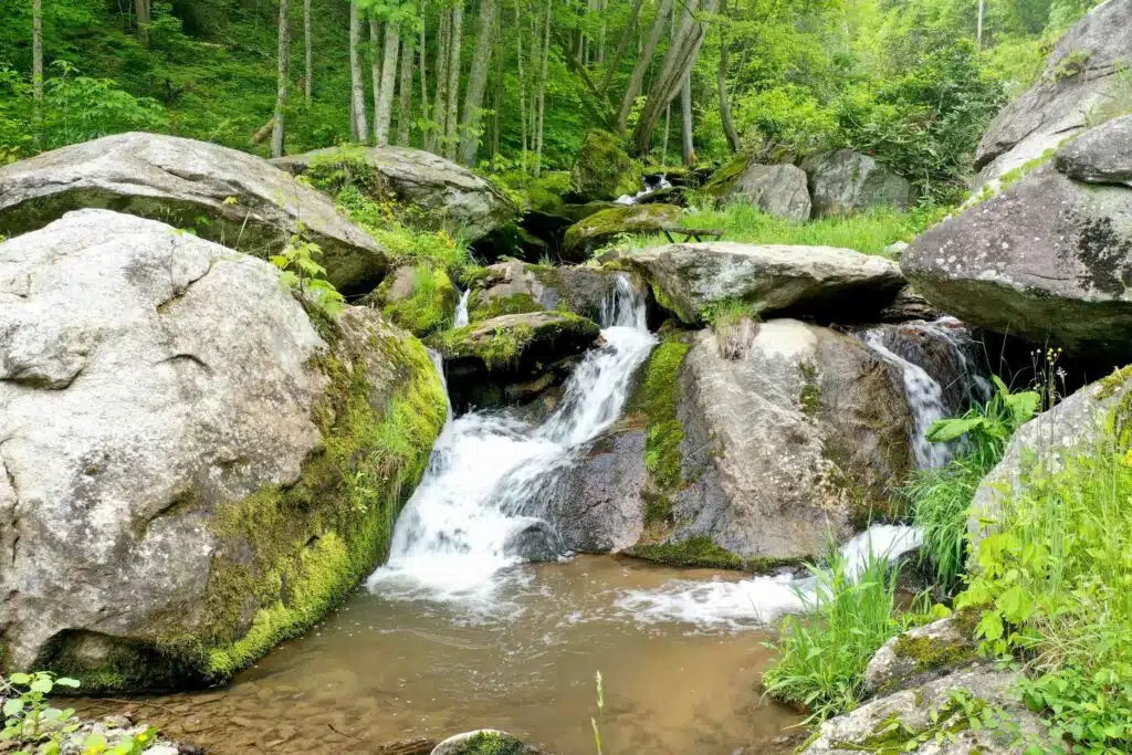 Dronephoto - flatrock from down in the pool Peaceful waterfall and woodland setting at Windows Over Waterfalls featuring boulders, rock formations, and lush green surroundings.