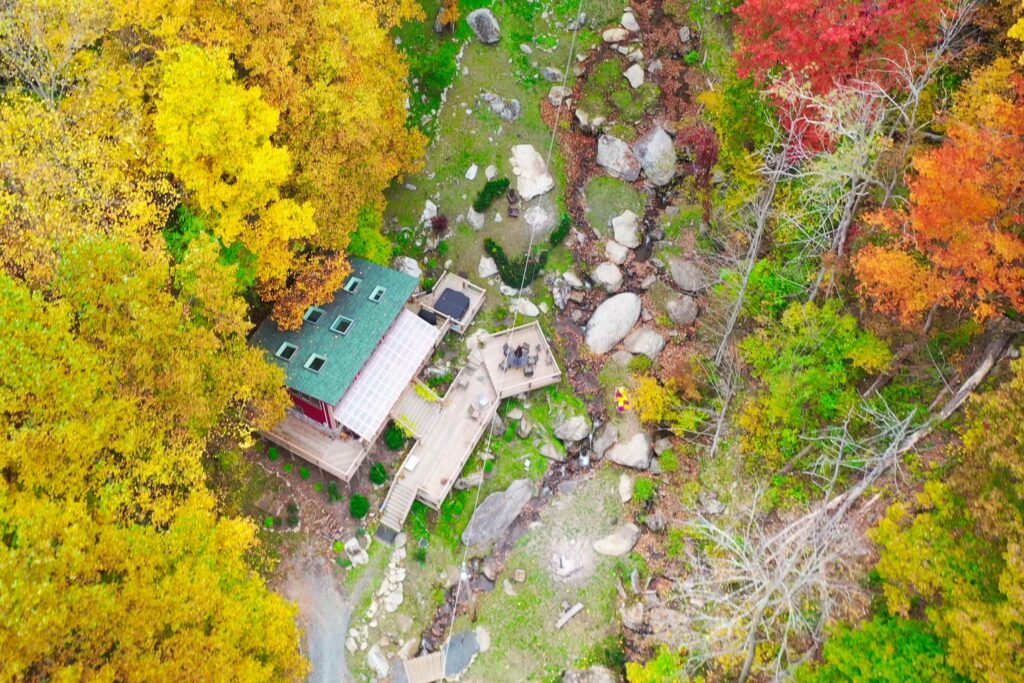 drone foliage above house looking down Cozy mountain cabin tucked into lush greenery with a waterfall stream below the deck