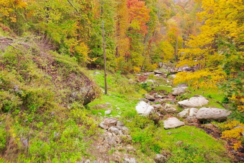 drone foliage flat above flat rock looking down Waterfall stream running past large boulders on a private cabin property in the Blue Ridge Mountains